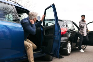 Senior and younger male drivers get out of cars and inspect damage after road traffic accident