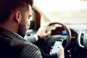 Man looking at mobile phone while driving a car.