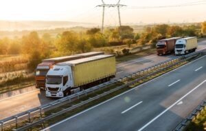 White and yellow semi trailer lorry truck overtaking red truck on a highway driving at beautiful dramatic sunset.