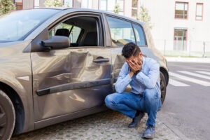 A car accident victim looking at a dent in his car. A Boston uninsured motorist car accident lawyer can help to ensure you get fair compensation